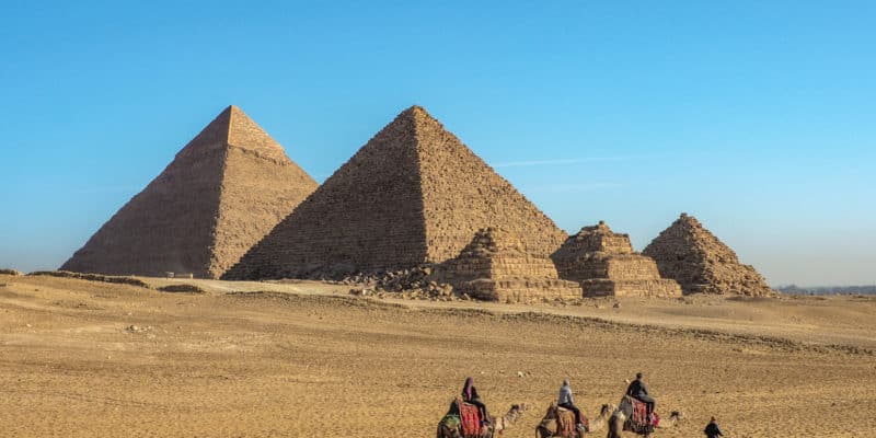 Turyści na wielbłądach przed trzema piramidami w Gizie