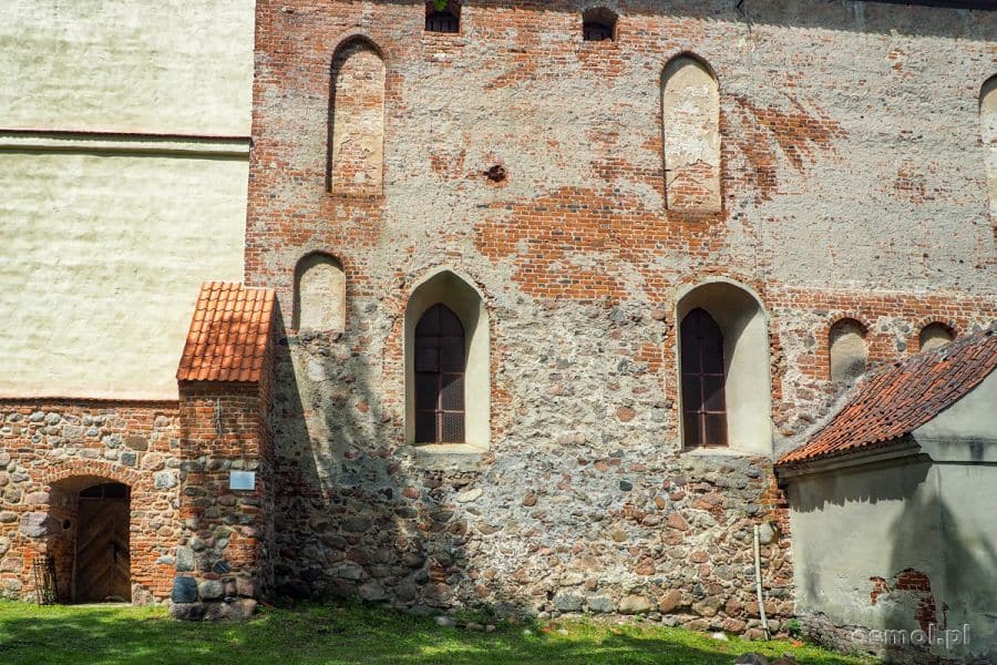 Kamienno-ceglany mur kościoła w Bezławkach. W lewej części zdjęcia widać kremowy mur dobudowanej kilka stuleci później kościelnej dzwonnicy.